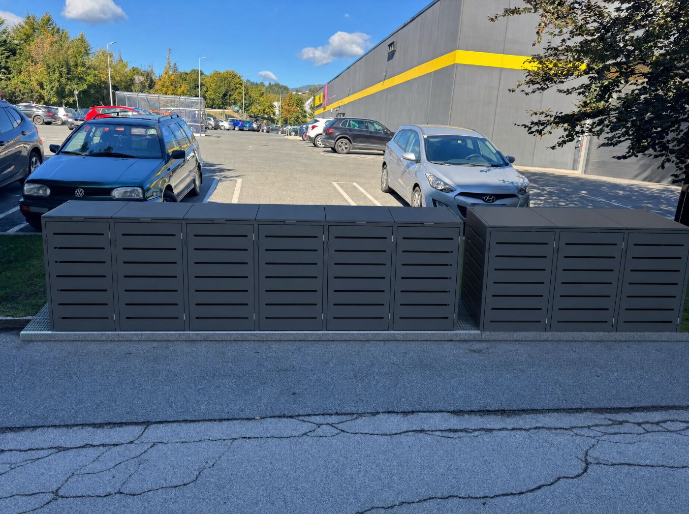Fotomontage: eine geschlossene anthrazitfarbene Box im Grünstreifen, die Fahrbahn davor ist frei.
